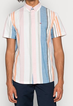 Homme portant une chemise à manches courtes à boutons avec des rayures verticales rose, bleu, gris, blanc et orange, assortie à un pantalon foncé.