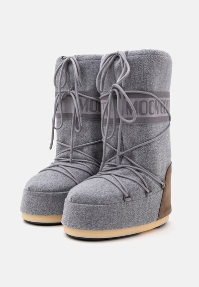 Paire de bottes d'hiver hautes grises avec des bouts arrondis, des semelles épaisses et des lacets croisés enroulés à l'avant et sur les côtés.