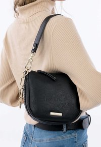 Czarna skórzana torba typu crossbody z teksturowaną powierzchnią, zakrzywionym kształtem i odczepianym paskiem z łańcuszka z złotymi akcentami. Zapięcie na zamek u góry.