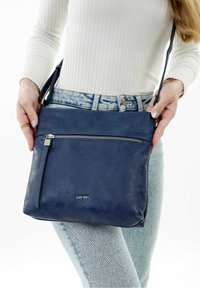 Borsa a tracolla in pelle perforata blu navy con dettagli in cerniera e tracolla regolabile. Presenta un logo sul davanti con finitura metallica.