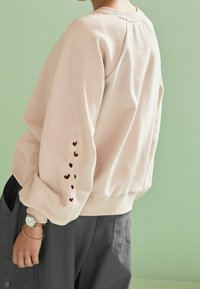 Felpa rosa chiaro con ritagli a forma di cuore sulle maniche, polsini a coste e scollatura rotonda. Tessuto morbido con una vestibilità comoda.