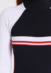 Top à rayures noir et blanc à col haut, avec des rayures horizontales rouge et blanche sur la poitrine. Design ajusté.