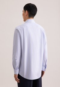 Koszula w paski w jasnoniebieskim i białym kolorze z mankietem na guziki, widok od tyłu z zakrzywionym dołem i gładką teksturą materiału.