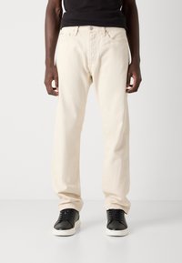 Béžové bavlněné džíny se rovnými nohavicemi, s zipem, pěti kapsami a viditelným šitím. V kombinaci s černými teniskami.