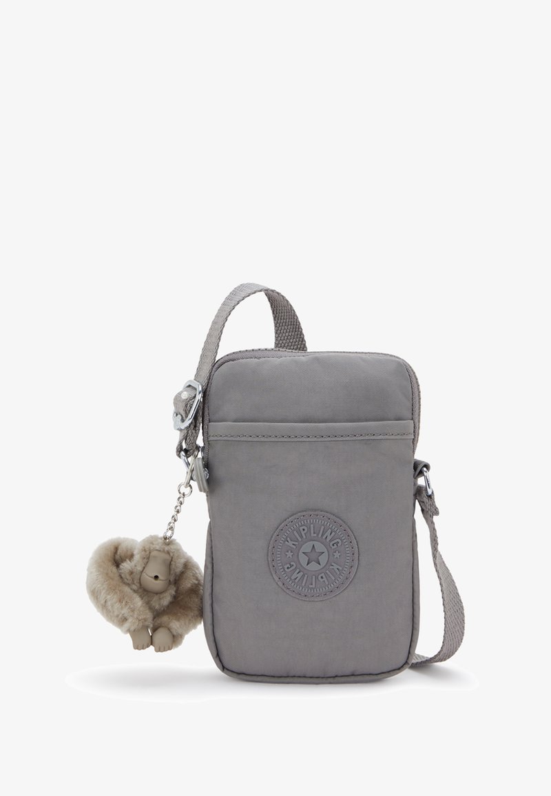Kleine graue Umhängetasche mit Kipling-Logo auf der Vorderseite und einem flauschigen Affen-Schlüsselanhänger, der an der Seite befestigt ist.