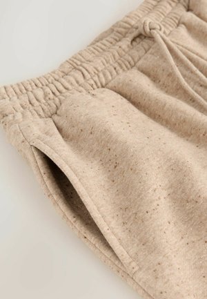 Pantaloni de trening bej, dintr-un material moale cu o textură granuloasă, dotati cu un brâu elastic și buzunare laterale.