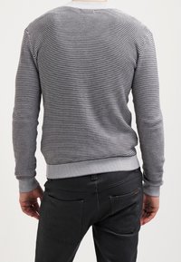Gray striped sweater with a ribbed crew neck and cuffs. The texture is knitted and the fit is slim, paired with black pants and pockets.