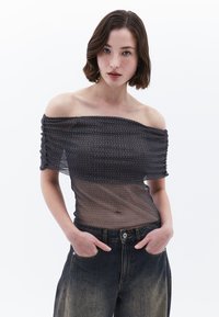 Sort gennemsigtig off-the-shoulder bluse med elastisk tekstur og sølvstribe mønster, parret med højtaljede denimjeans.