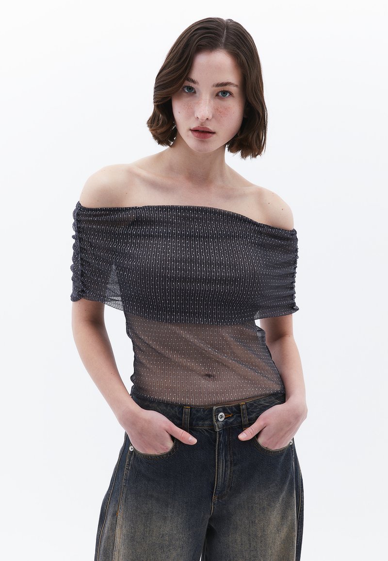 Sort gennemsigtig off-the-shoulder bluse med elastisk tekstur og sølvstribe mønster, parret med højtaljede denimjeans.
