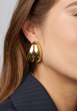 Gouden metalen hoepeloorbellen met een gladde, gepolijste afwerking, met een dikke, ronde ontwerp dat dicht bij het oor zit.
