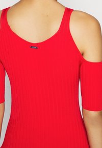 Robe rouge côtelée avec des manches dénudées, un décolleté en arrière arrondi et une petite étiquette de la marque près du centre du dos.