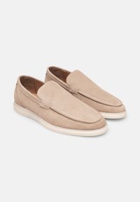 Beige suède loafers met een gladde afwerking, ronde neus en een gestikte naad langs de rand. Witte rubberen zool voor demping.