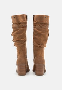 Bottes en daim marron jusqu'au genou avec un design lâche, présentant des coutures décoratives et un talon bloc. Fermeture éclair sur le côté.
