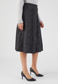 Een zwarte, knie-lange rok met een textuurpatroon van abstracte vormen. Gecombineerd met zwarte puntige hakken.