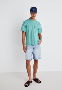 Lys blå bomull t-skjorte, korte ermer, kombinert med lyse denimshorts og brune sandaler. Marineblå caps med logo. Enkel, uformell antrekk.