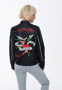 Giacca di pelle nera con un vivace design ricamato di un uccello, un cuore e il testo "TRUE TIL DEATH" sul retro. Accenti laterali bianchi.
