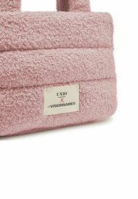 Borsa rosa texturizzata con un esterno in peluche, manici doppi e un'etichetta con il logo "UNIO HAMBURG X LES VISIONNAIRES." Materiale morbido e peloso.