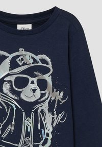 Marineblaue Sweatshirt mit einem glänzenden silbernen Grafik eines Bären, der Sonnenbrillen, eine Baseballmütze und eine Jacke trägt, mit geschwungener Schrift.