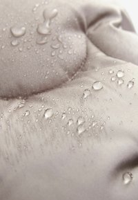 Vandafvisende polstret stof med en glat, lys grå tekstur. Viser dråber af vand på overfladen, hvilket fremhæver dets vandtætte egenskaber.