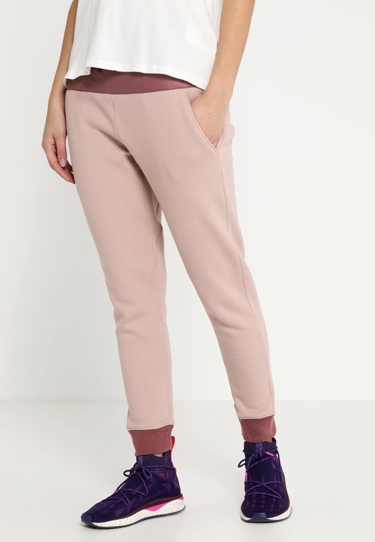 Rosa sweatpants med ribbade muddar, sidofickor och en slät yta. Kombineras med lila träningsskor med mönstrade accenter.