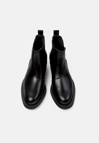 Botines de cuero negro con un acabado suave, puntera redondeada, paneles laterales elásticos y una lengüeta en la parte posterior para facilitar su uso. Suela de goma plana.