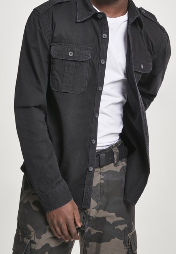 Svart långärmad skjorta i bomull med två bröstfickor, knäppning med knappar och krage. Tillsammans med kamouflage cargo-byxor.