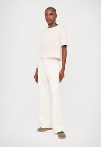 Tricou scurt roz deschis cu mâneci scurte, asortat cu pantaloni albi, cu talie înaltă și lățimi ample. Modelul poartă adidași verzi măslinii.