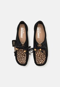 Pantofi din suede negru, stil mocasin, cu un superior cu imprimeu leopard, șireturi negre cu mărgele din lemn și o branț bej cu logo-ul brandului.