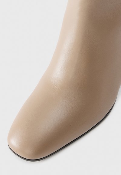 Beige leather ankle boot with a smooth finish, square toe design, and subtle stitching details. Black sole accentuates the base.