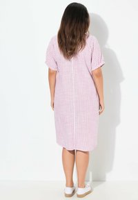 Gestreepte midi-jurk in roze en wit, met korte mouwen, een ontspannen pasvorm en een gebogen zoom. Gepaard met witte instapschoenen.