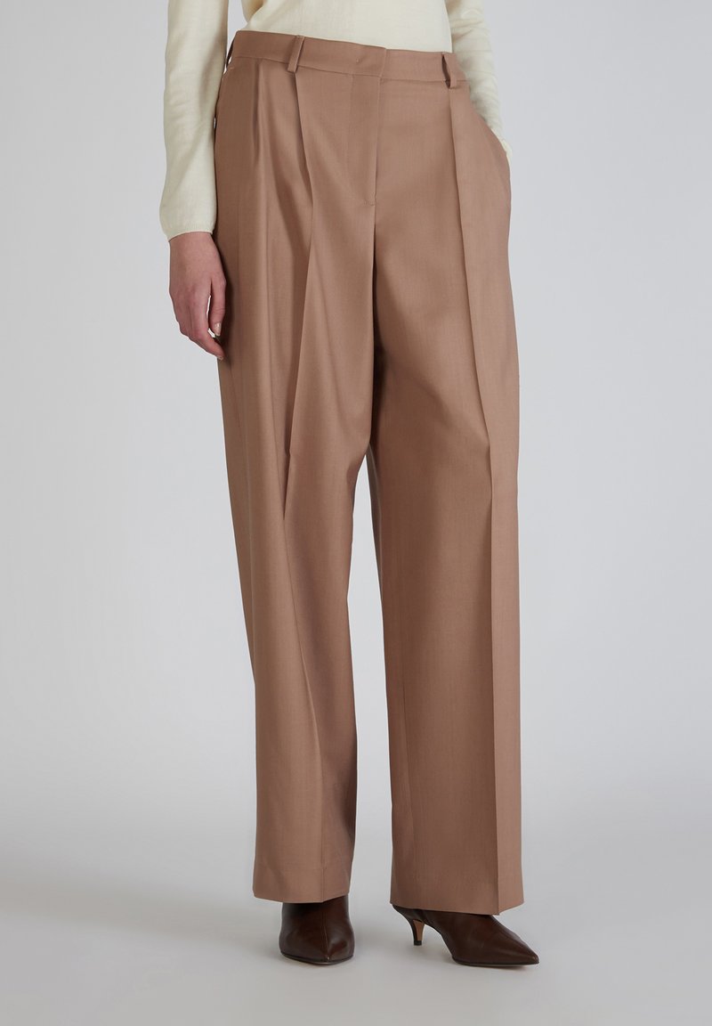 Bruine op maat gemaakte broek met plooien, gemaakt van gladde stof, met een hoge taille, rechte pijpen en zijzakken, gecombineerd met puntige hakken.