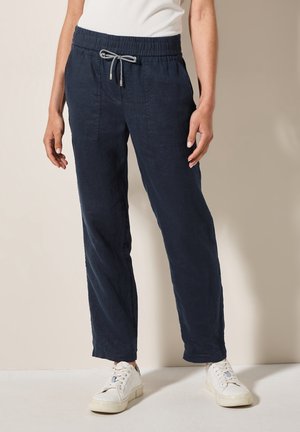 Pantalones de lino azul marino con cordón, de corte holgado, que cuentan con dos bolsillos laterales y una cómoda pretina elástica, combinados con zapatillas blancas.