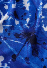 Tessuto blu a fantasia con schizzi di nero e bianco, caratterizzato da una trama liscia e da un design astratto, che ricorda un effetto tie-dye.