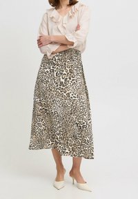 Jupe midi en imprimé léopard beige et noir, avec un tissu lisse et léger et une silhouette fluide. Associée à un chemisier rose à volants.