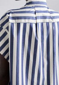 Short-sleeve shirt featuring alternating navy blue and white vertical stripes. Tailored collar and pleated back detail. Cotton fabric.