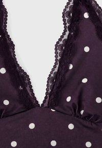 Tissu noir à pois blancs, doté d'un décolleté en V orné d'une délicate dentelle noire.