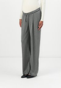 Graue weite Hosen aus weichem Stoff, mit einem elastischen Bund und Kordelzug sowie lockerer Passform. Kombiniert mit schwarzen spitzen Schuhen.