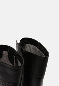 Botas negras de tobillo con un exterior de cuero suave, cierre de cremallera y forro gris suave. Presentan detalles de costura y paneles elásticos en los laterales.