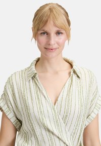 Lekka, kremowa koszula w zielone pionowe paski, z dekoltem w kształcie litery V i podwiniętymi rękawami, wykonana z teksturowanej tkaniny.