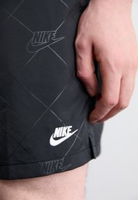 Sorte shorts med diamantmønster, prydet med hvide Nike-logo accenter. Fremstillet af letvægtsmateriale med en glat tekstur.