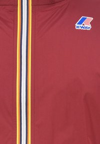 Chaqueta K-Way en burdeos con cremallera frontal. Presenta un patrón a rayas en amarillo, blanco y marino. Incluye un detalle de logo en el pecho.