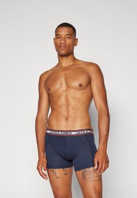 Navy boxer briefs with a wide elastic waistband featuring "JACK & JONES" in contrasting colors. Smooth texture, fitted design.