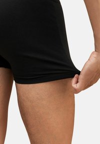Una persona tira il bordo di pantaloni neri aderenti all'altezza della coscia, mostrando l'elasticità e la texture del tessuto.