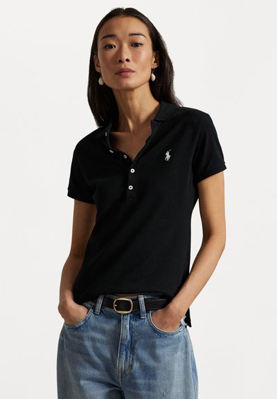 Zwarte polo gemaakt van katoen, met een knoopsluiting van drie knopen, korte mouwen en een klein geborduurd logo. Gecombineerd met lichtblauwe denim jeans.