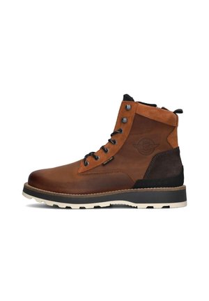 Botte cheville en cuir marron avec un dessus en daim, des accents noirs, des œillets en métal et une semelle en caoutchouc blanche avec un profil texturé.