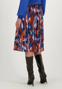 Jupe évasée colorée dans des teintes de rouge, de bleu et de rose avec un motif de tissu fluide ; assortie à des bottes en cuir noir jusqu'aux genoux.