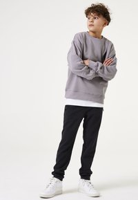 Grijze sweatshirt met verlaagde schouders, gecombineerd met zwarte slim-fit broek met ritszakken en witte hoge sneakers.