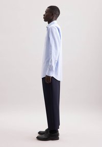 Camicia a quadri azzurro chiaro con colletto abbottonato, maniche lunghe e taglio dritto, abbinata a pantaloni scuri su misura e scarpe nere.