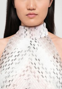 Top cu guler halter, realizat dintr-un material cu un model complex, cu un gradient de roz deschis spre alb, accentuat de desene geometrice negre.