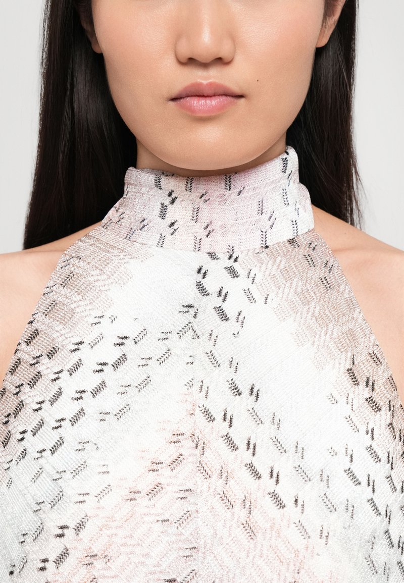 Haut à col halter en tissu à motif complexe avec un dégradé de rose pâle à blanc, accentué par des motifs géométriques noirs.